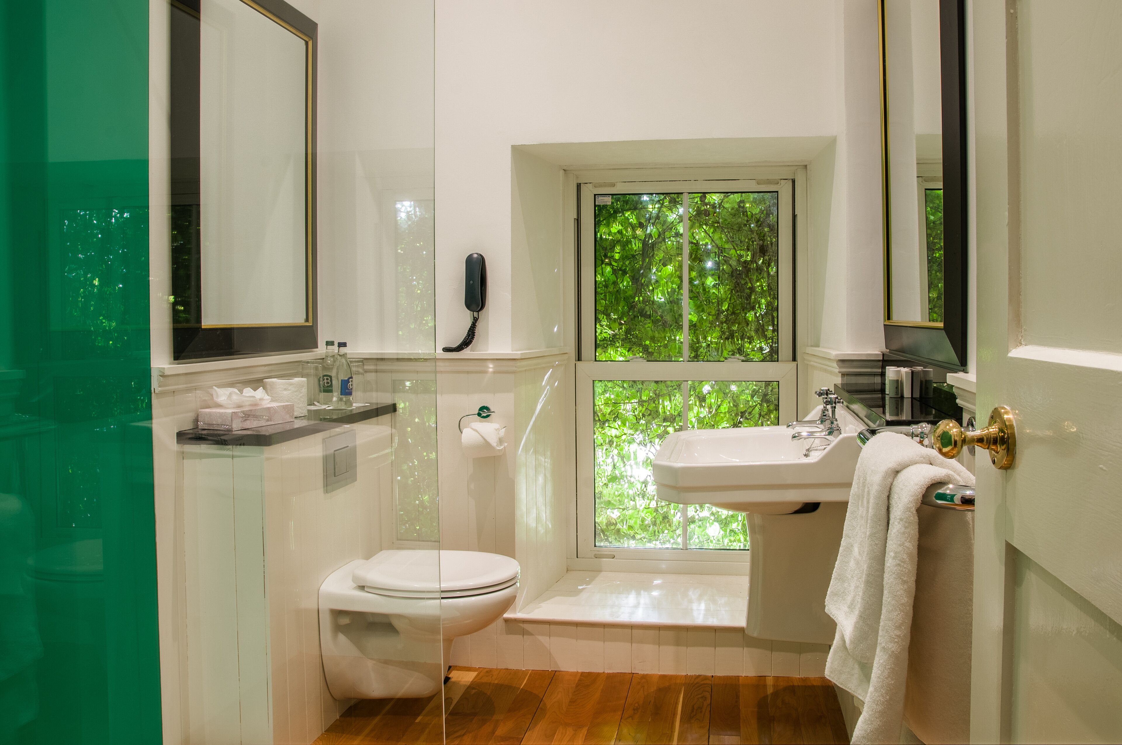 A bathroom with a toilet, sink, and a window with a view of greenery.