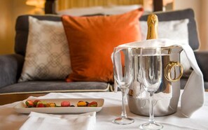 A champagne bottle, two wine glasses, and a plate of macarons on a table in a hotel room.