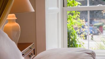 Un dormitorio con cama, mesita de noche, lámpara y ventana con vista a la vegetación.