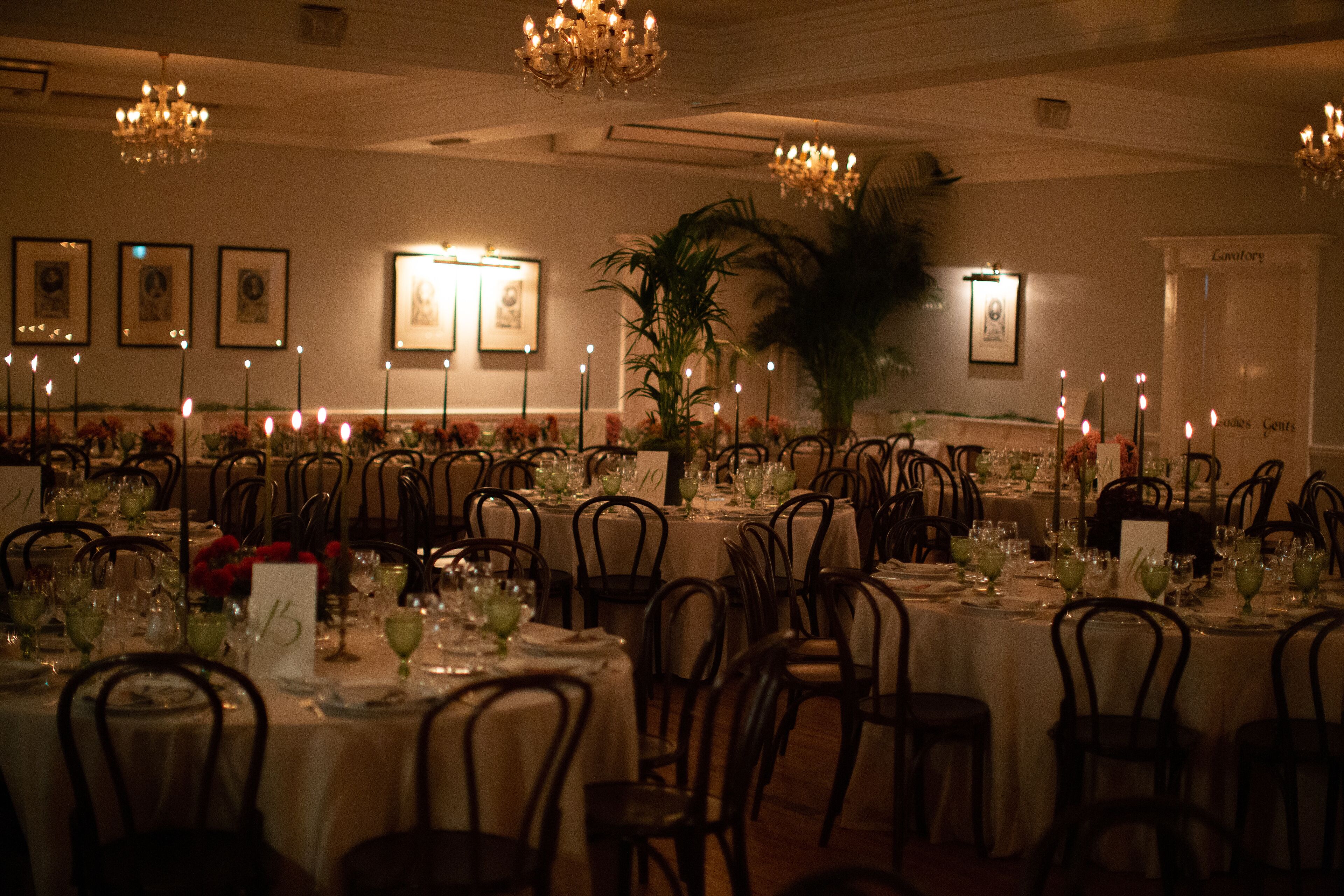 A formal dining room with multiple tables set for a meal, each with chairs, glassware, and a centerpiece.