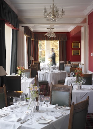 A formal dining room with multiple tables set for service, elegant chairs, and a chandelier.