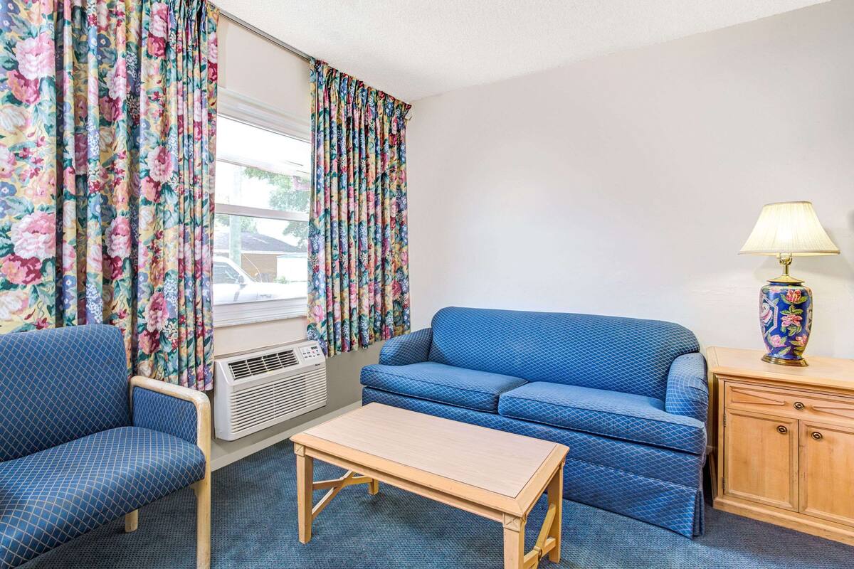 A room with a blue sofa, a wooden table, a lamp, and a floral curtain.