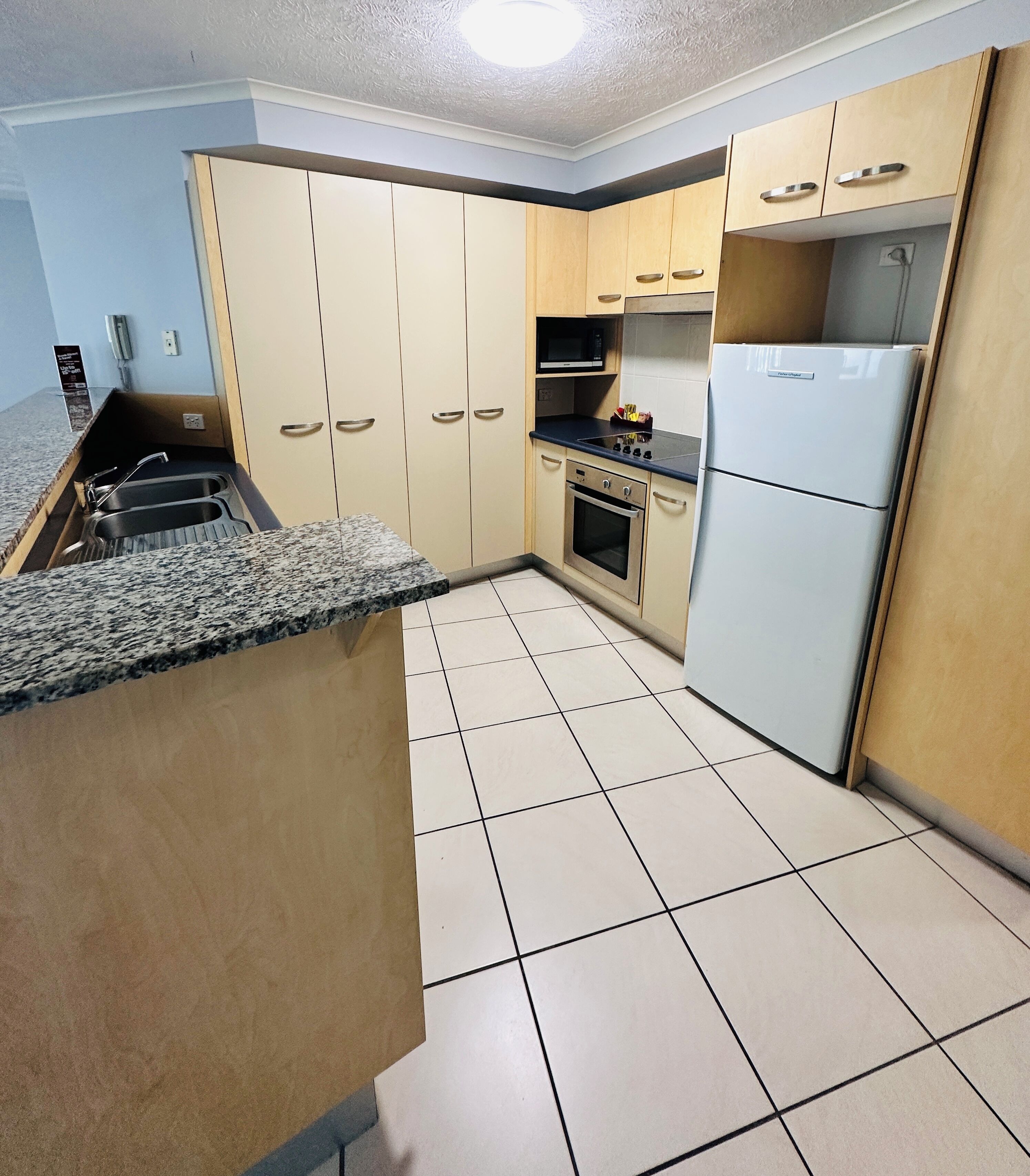 A kitchen with a granite countertop, a refrigerator, an oven, and wooden cabinets.