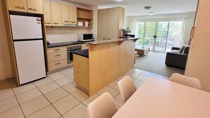 Une cuisine moderne dotée d’un îlot central, un coin repas avec une table et des chaises, et un espace de vie comprenant un canapé et un balcon.