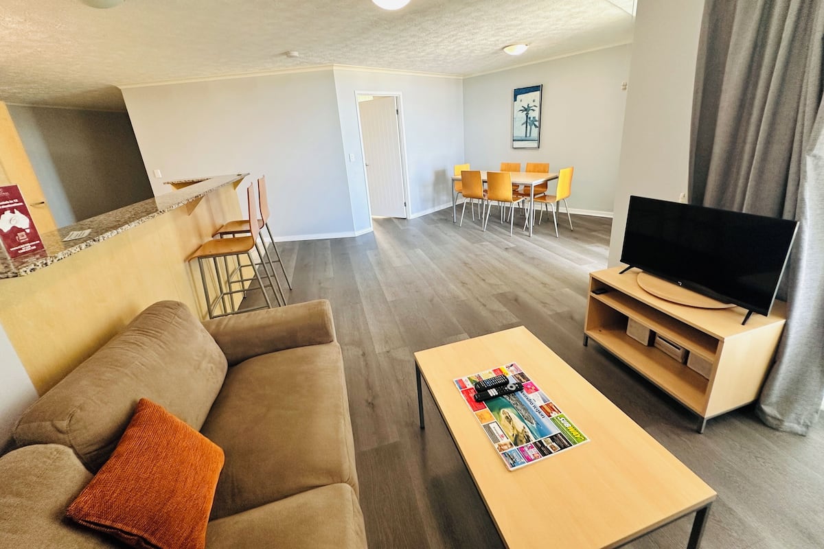 Una sala de estar moderna con sofá, mesa de centro, televisor, comedor y cocina.