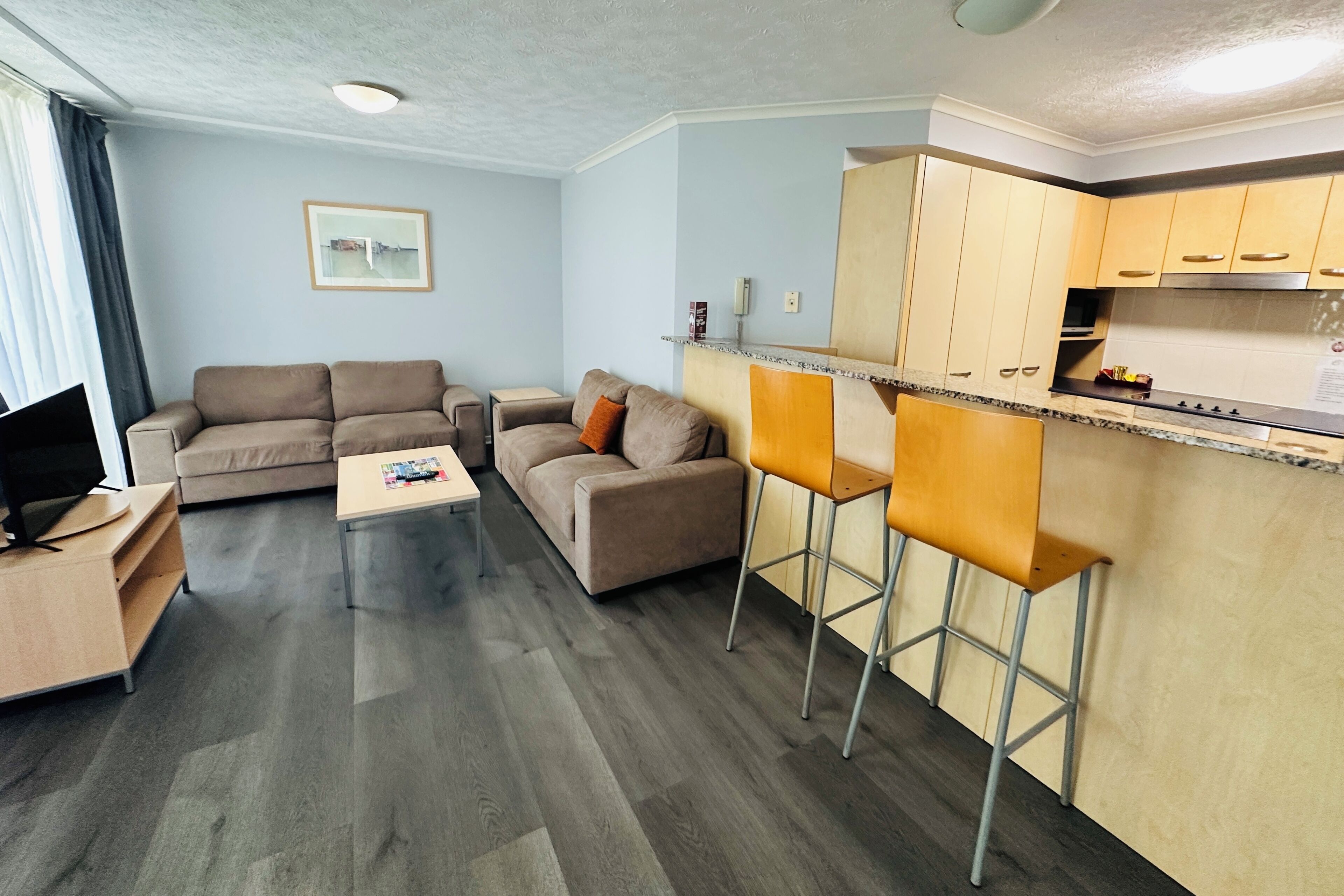 Un salon moderne avec un canapé, une table basse et un meuble pour la télévision. Il y a également un coin cuisine avec un comptoir et des tabourets de bar.