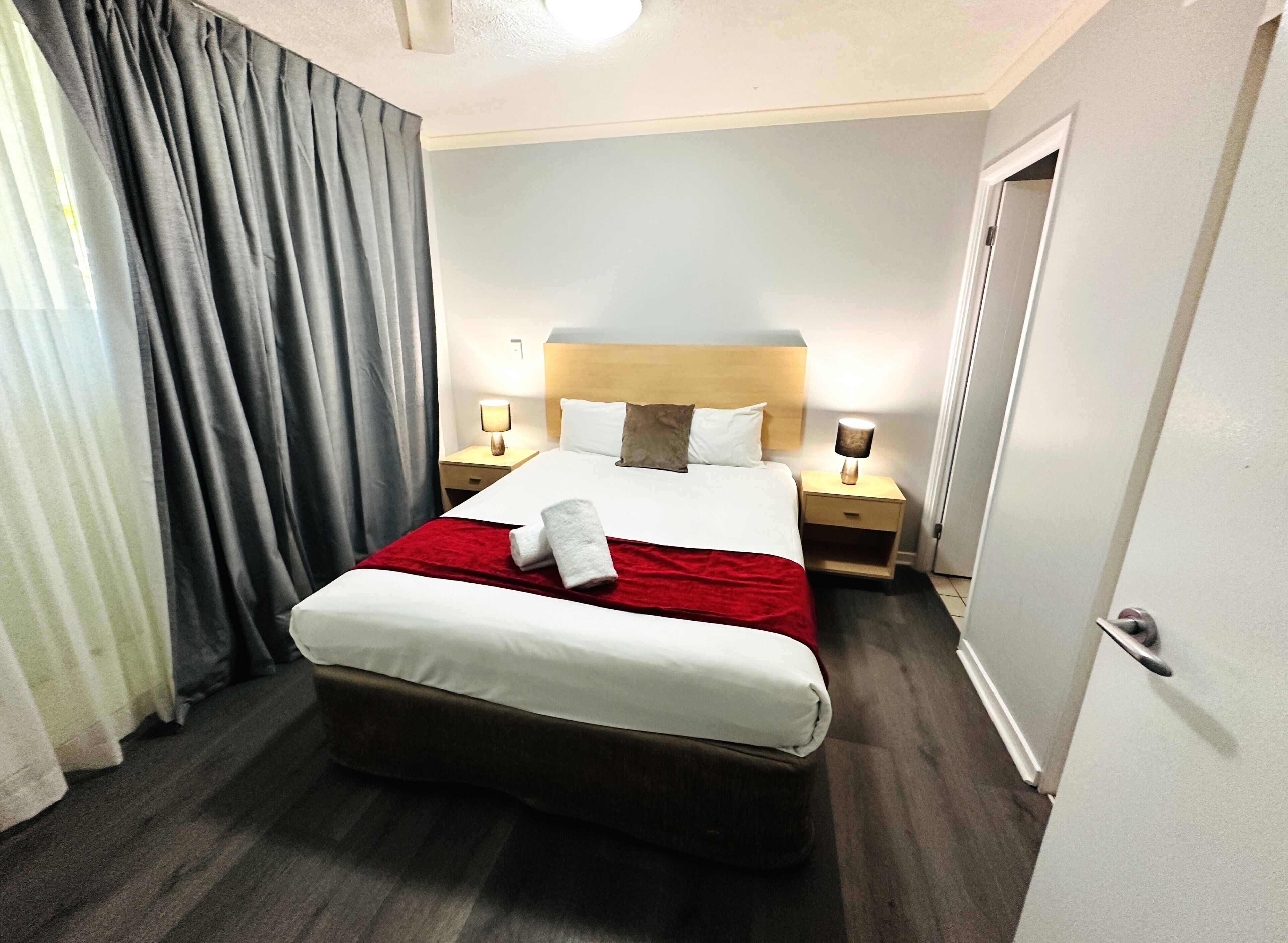 A hotel room with a bed, two bedside tables, a headboard, and a door.