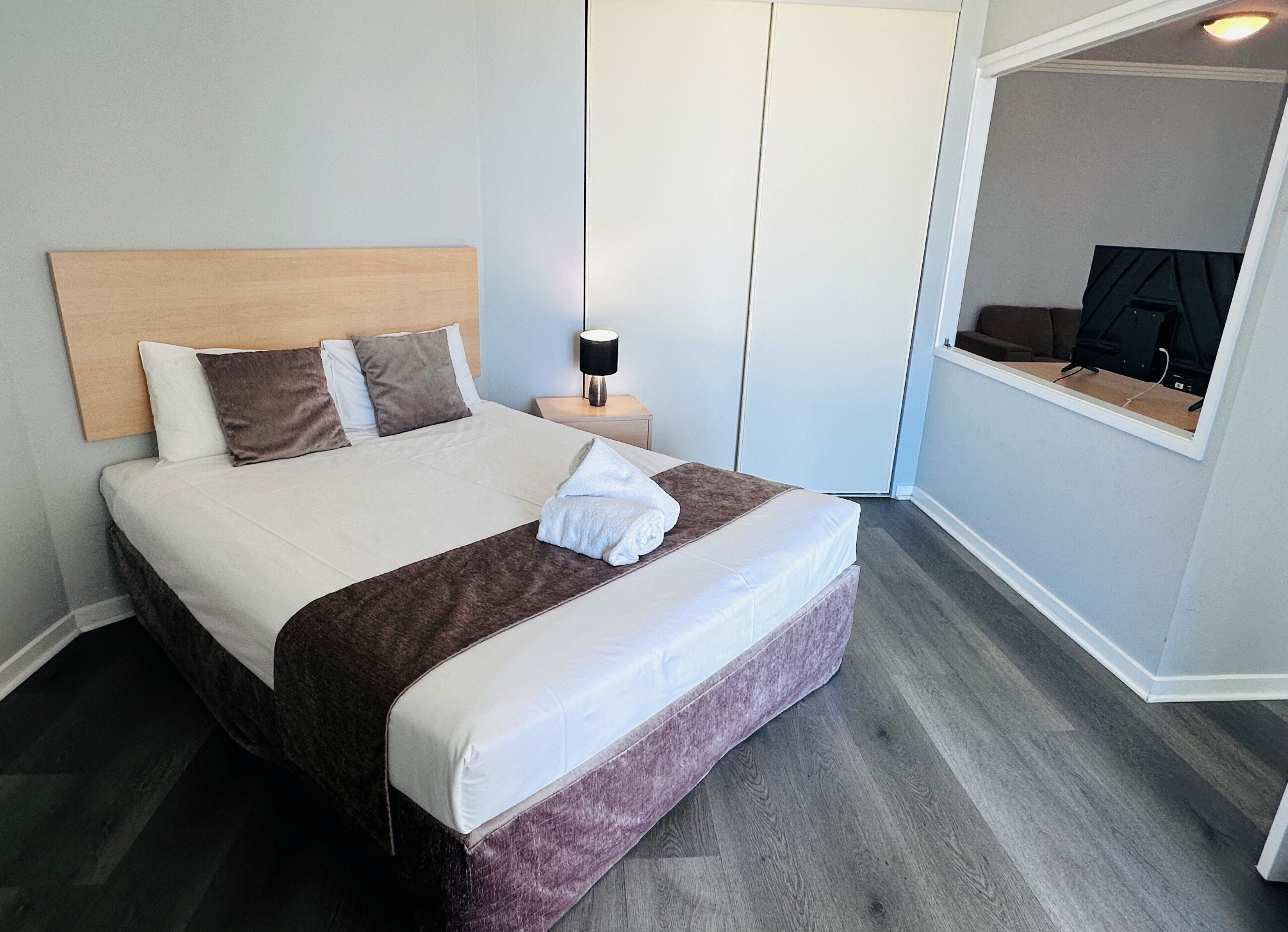 A neatly made bed with a headboard, a bedside table with a lamp, and a wall-mounted TV.