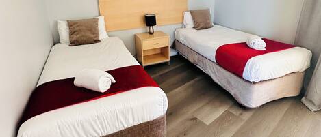Habitación de hotel con dos camas, una mesita de noche, un cuadro enmarcado en la pared y suelo de madera.