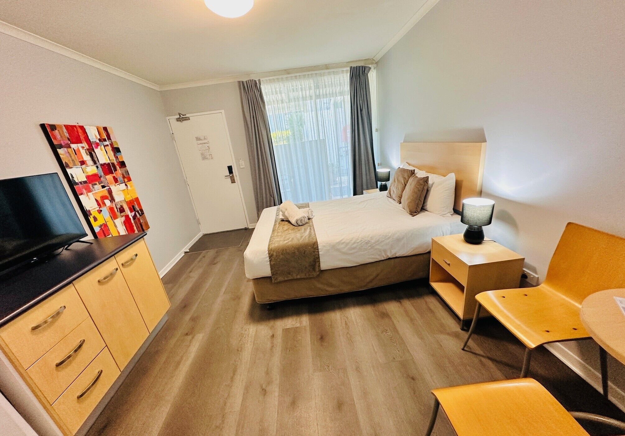 Une chambre d’hôtel avec un lit, une table de chevet, une lampe, une télévision et un tableau au mur.