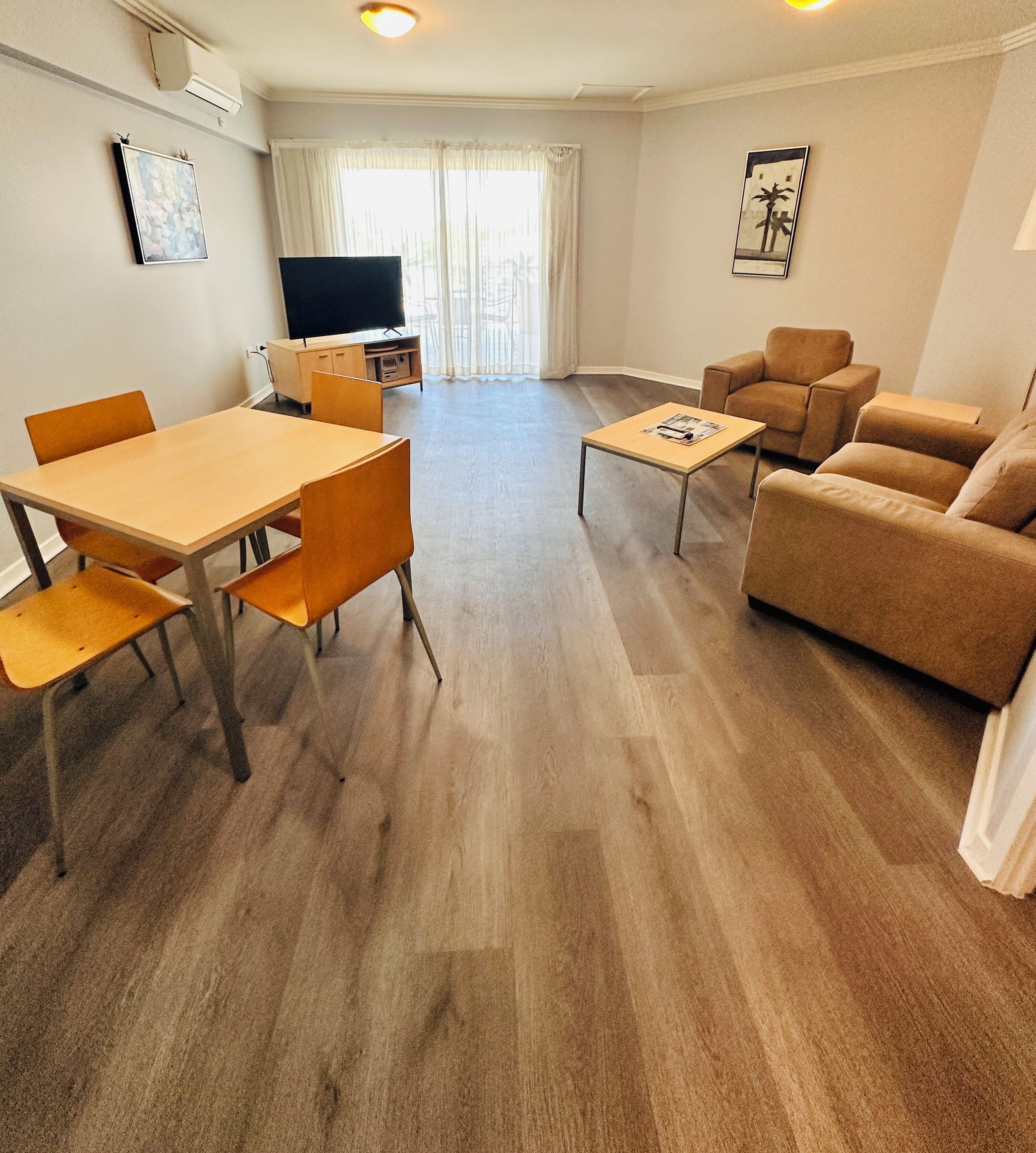 Un salon comprenant un canapé, des fauteuils, une table basse, un téléviseur et une table à manger.