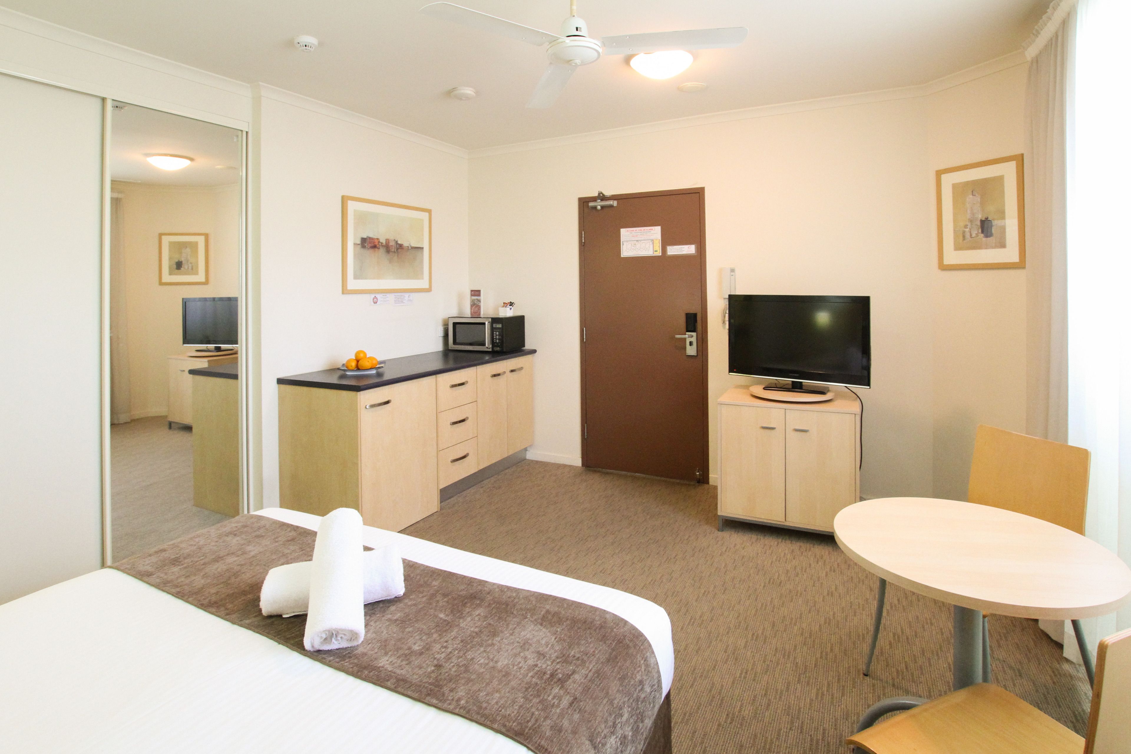 A hotel room with a bed, a desk, a television, a microwave, and a door.