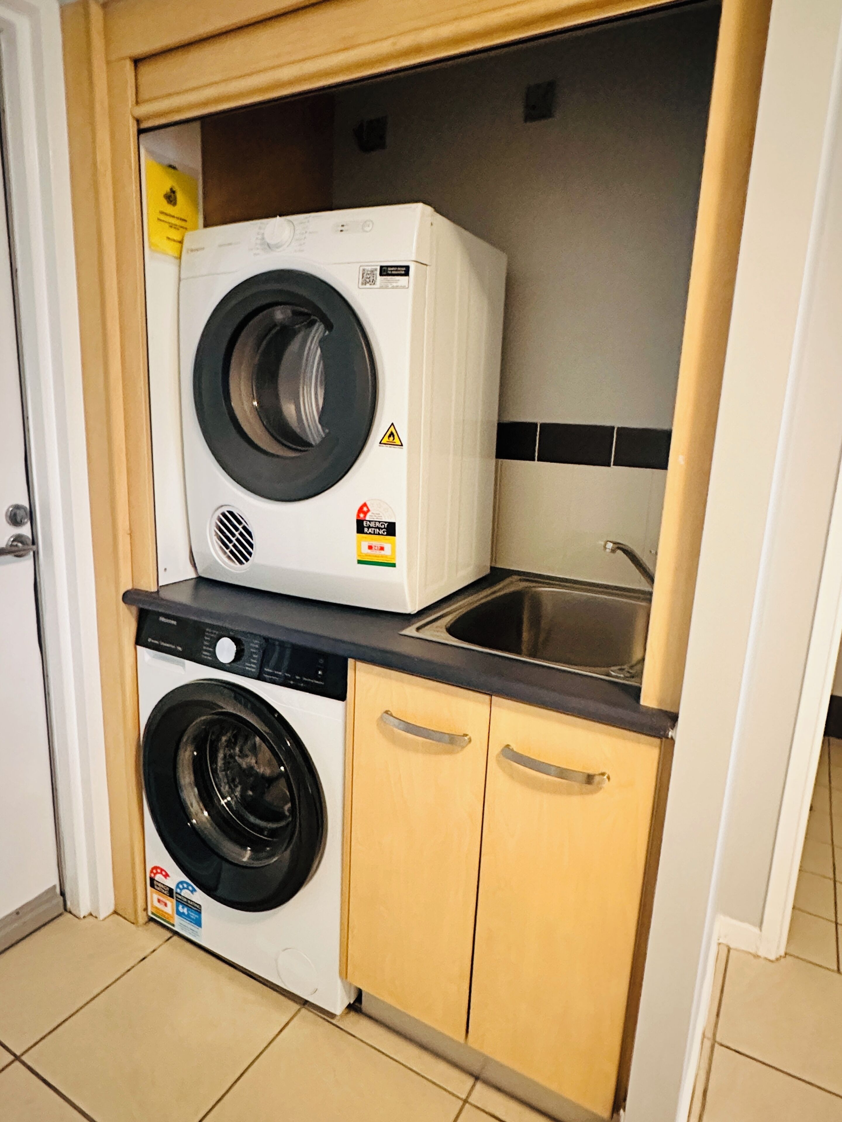 Un espace buanderie compact comprenant un lave-linge et un sèche-linge à chargement frontal, un évier et des armoires en bois.