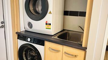 Un espace buanderie compact comprenant un lave-linge et un sèche-linge à chargement frontal, un évier et des armoires en bois.