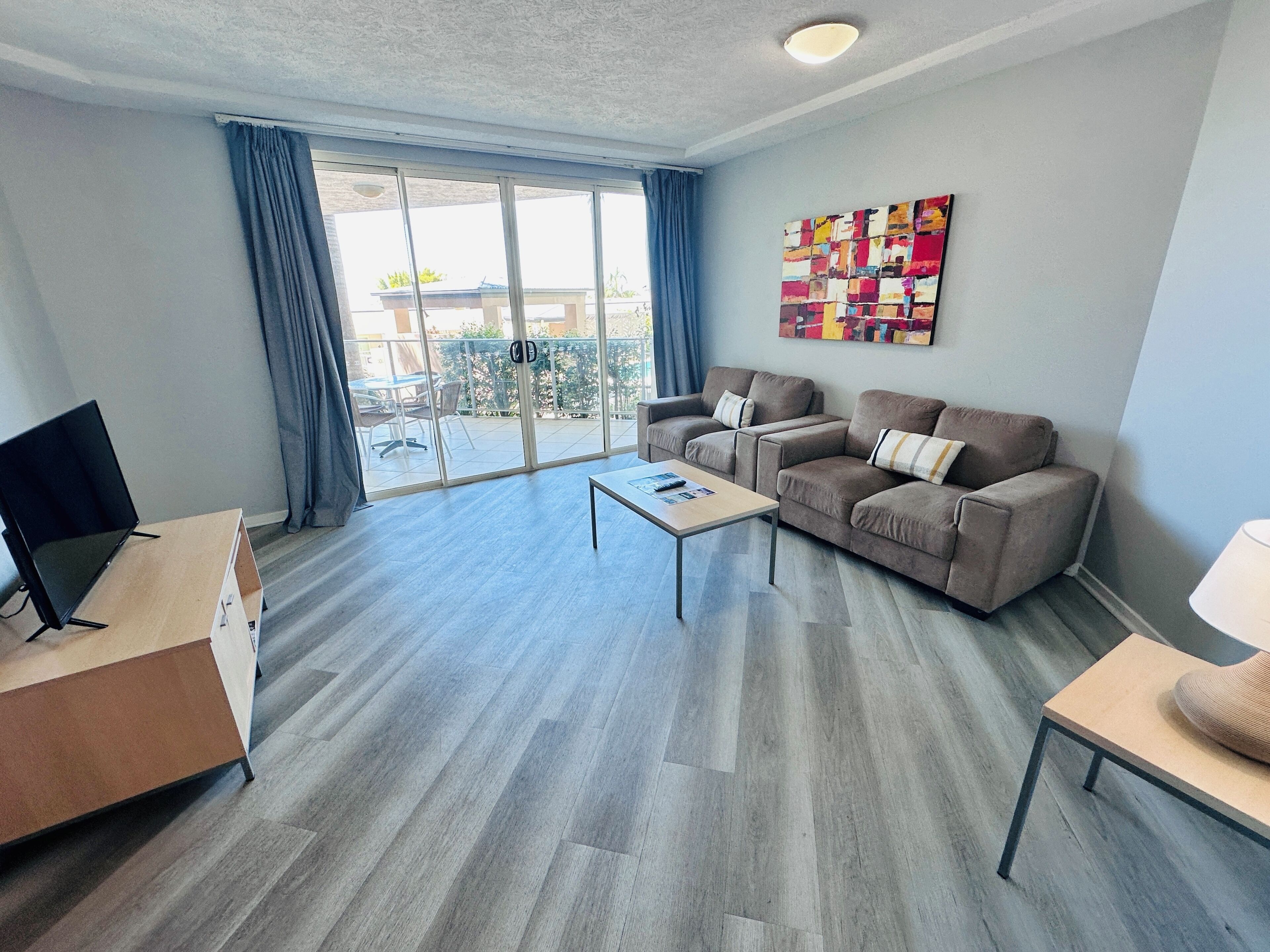 A modern living room with a sofa, coffee table, TV, and a balcony with curtains.