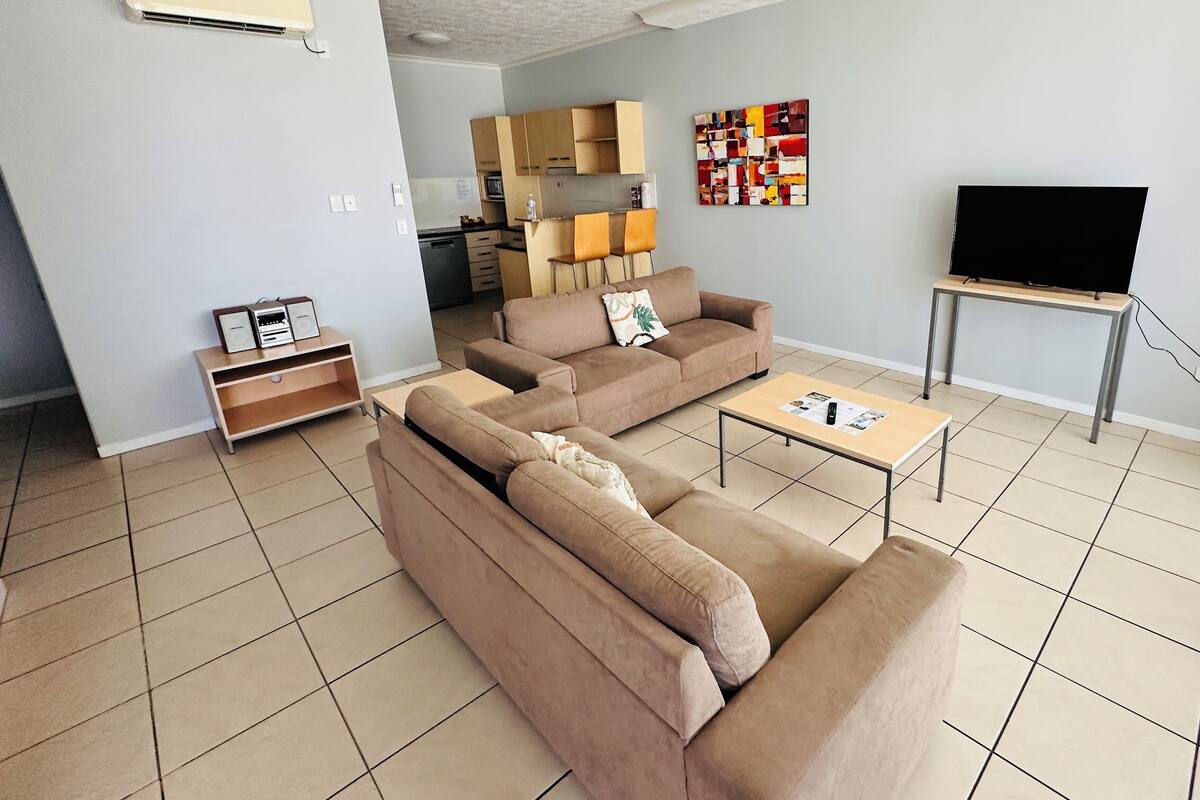 Una sala de estar con sofá, mesa de centro, televisor y cocina al fondo.
