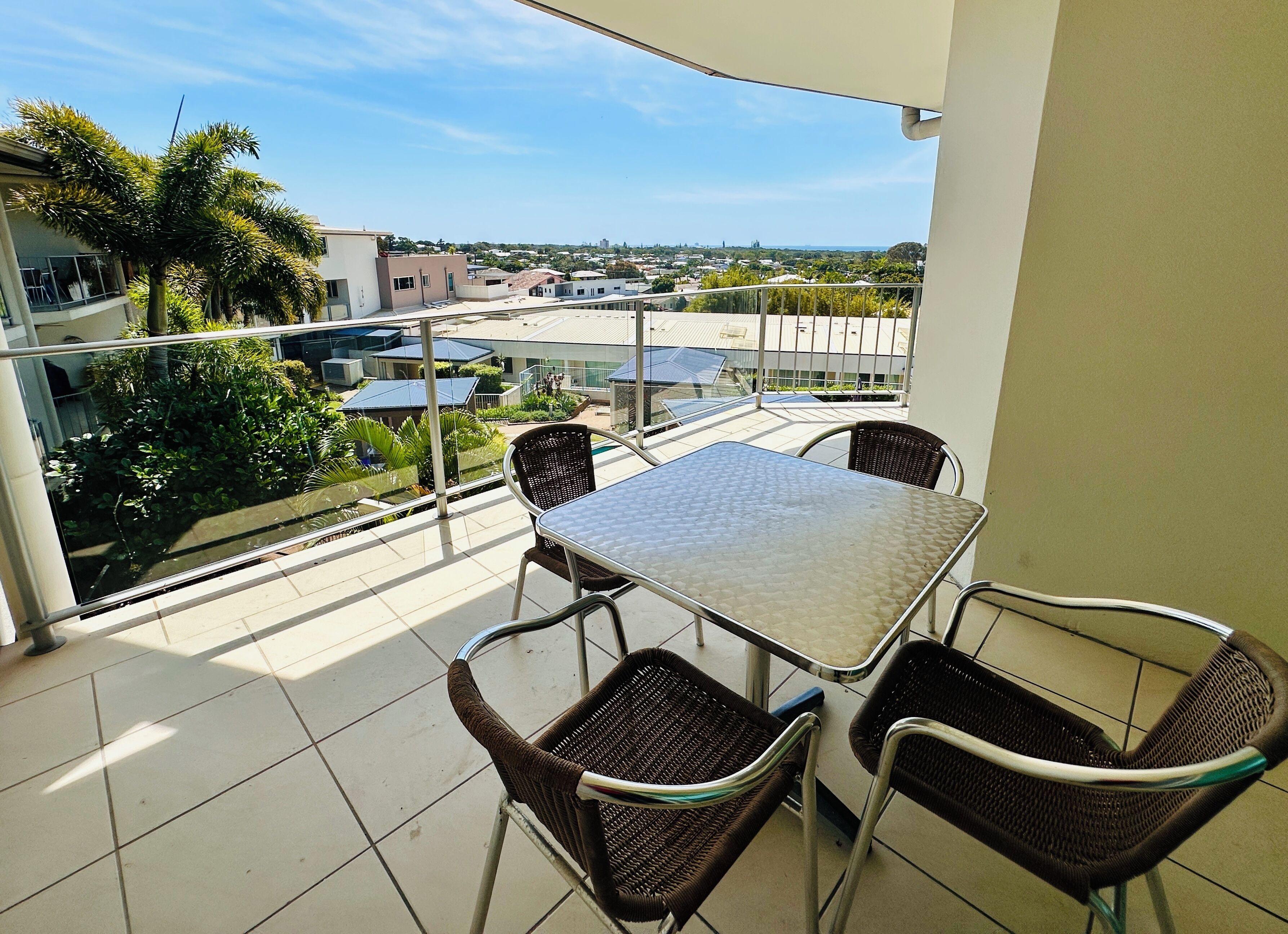 A balcony with a table and chairs, overlooking a residential area with houses and greenery.