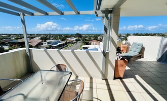 Un balcón con vistas a una zona residencial, una silla, una mesa y una planta en maceta.