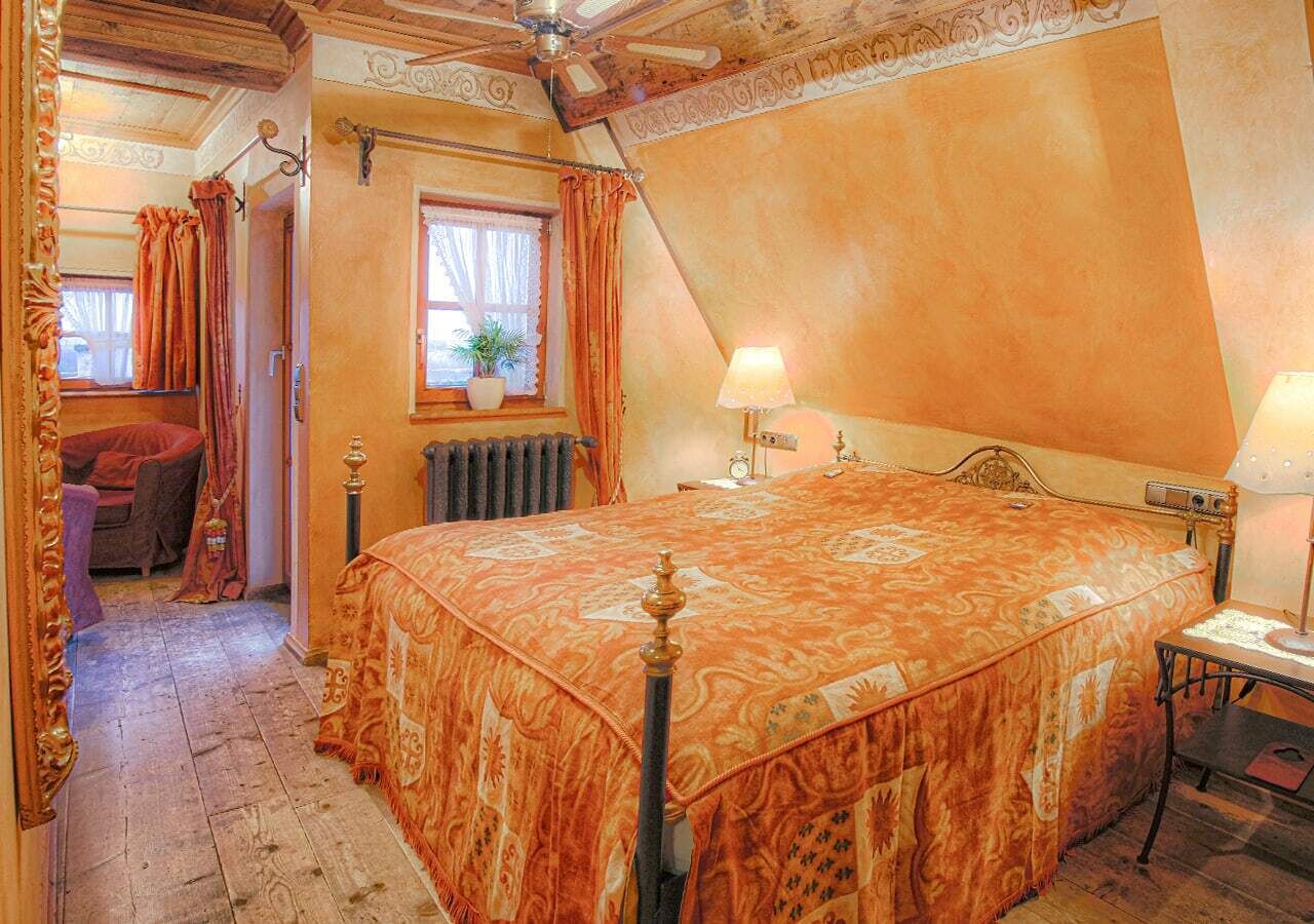 Slaapkamer met een groot bed, nachtkastje, lamp, raam met gordijnen, radiator en een stoel.