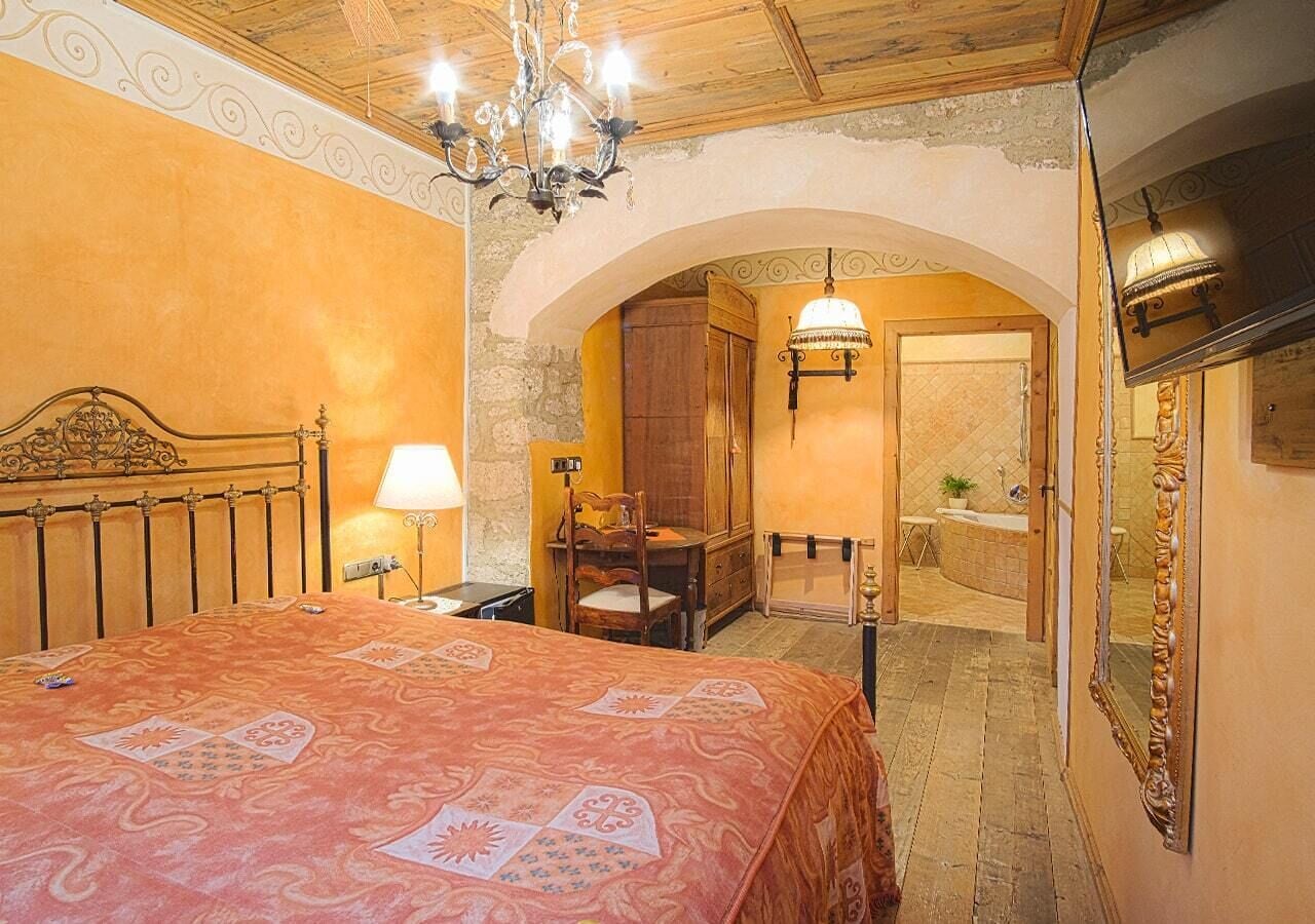 Une chambre à coucher avec un grand lit, un lustre, une armoire en bois et une salle de bain visible à travers une arche.