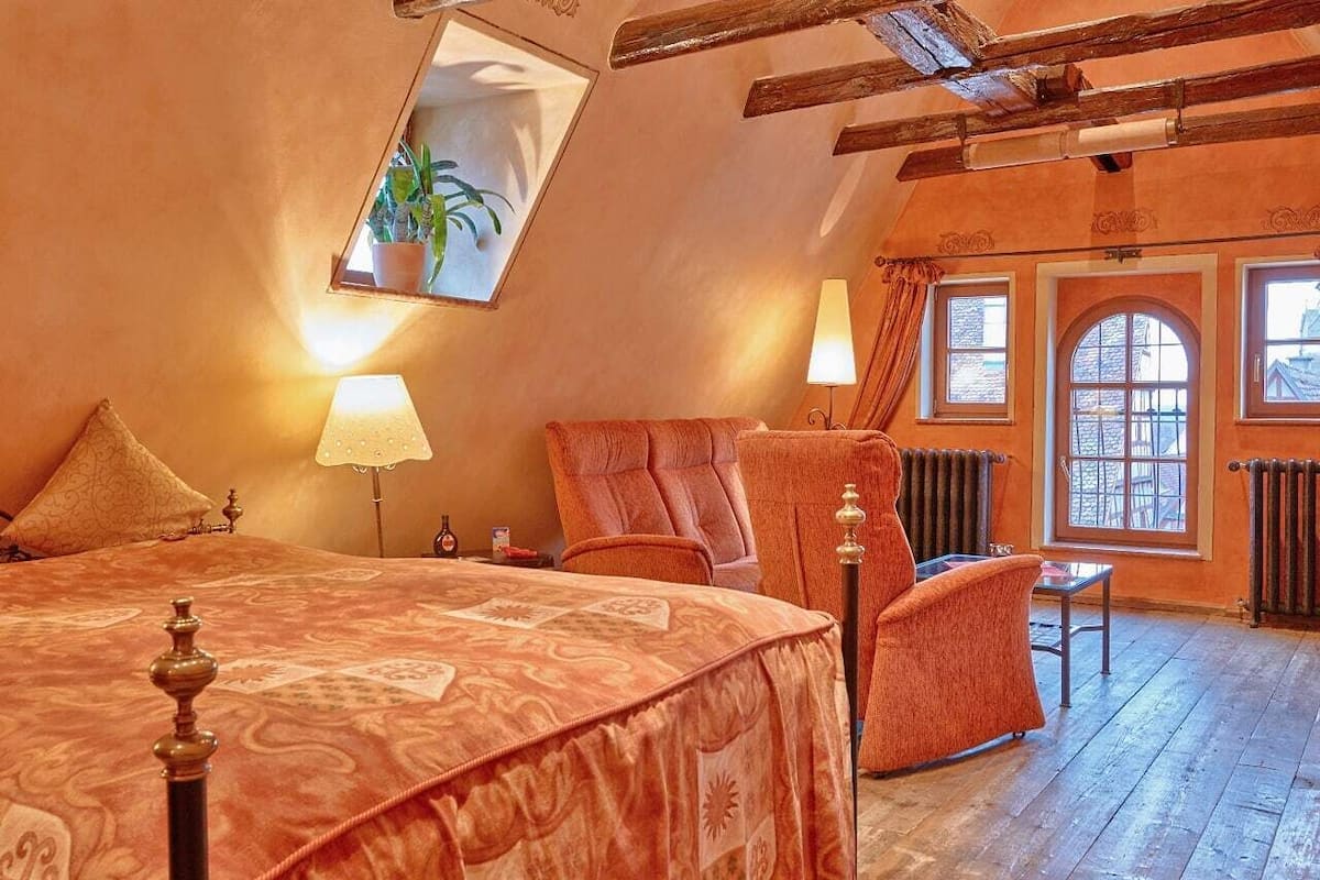 A bedroom with a large bed, a chair, a table, and a window with a view.