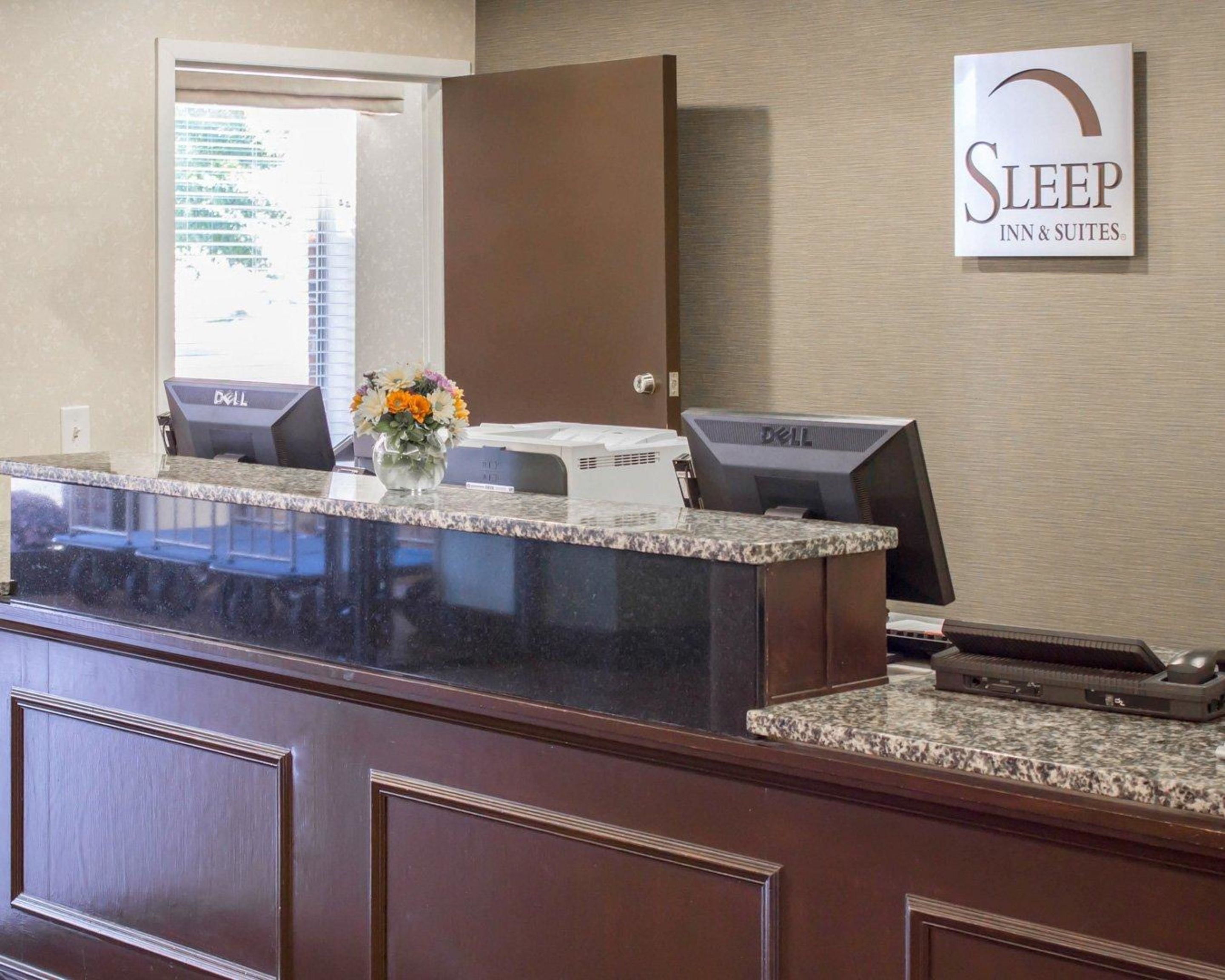 A reception desk with a computer, a vase with flowers, and a sign for Sleep Inn & Suites.