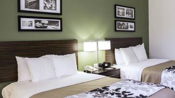 A hotel room with two beds, a nightstand with a lamp, and framed pictures on the wall.