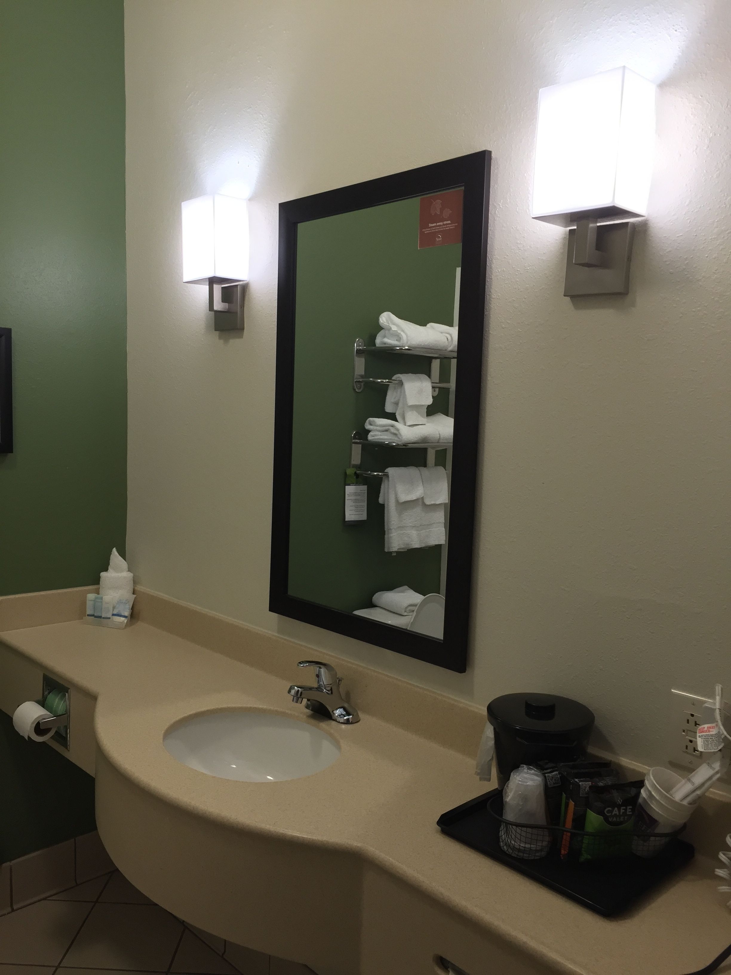A bathroom with a sink, mirror, towel rack, and toiletries.