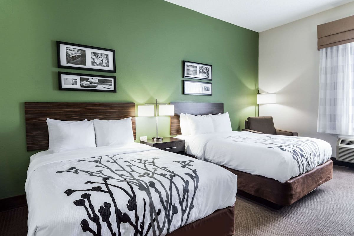 A hotel room with two beds, green walls, framed pictures, a lamp, and a window with curtains.