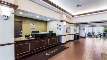 A hotel reception area with a reception desk, a welcome mat, and a seating area with tables and chairs.