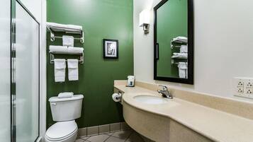 A bathroom with a green wall, a white toilet, a beige sink, and a mirror.