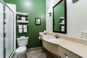 A bathroom with a green wall, a white toilet, a beige sink, and a mirror. - Sleep Inn & Suites Smithfield near I-95 (Smithfield)