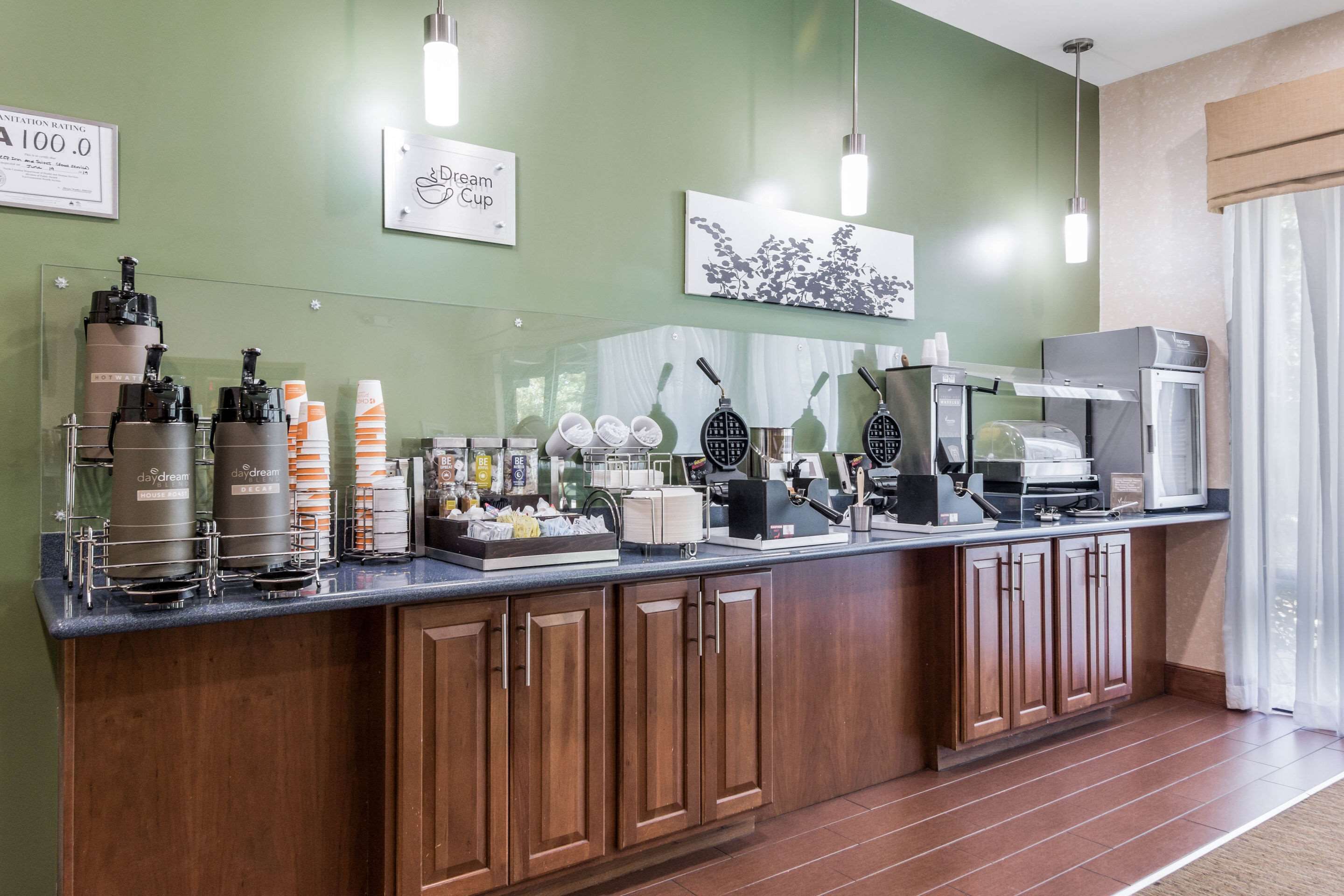 Una barra de desayuno con máquinas de café, un fabricante de gofres y diversas opciones de comida.