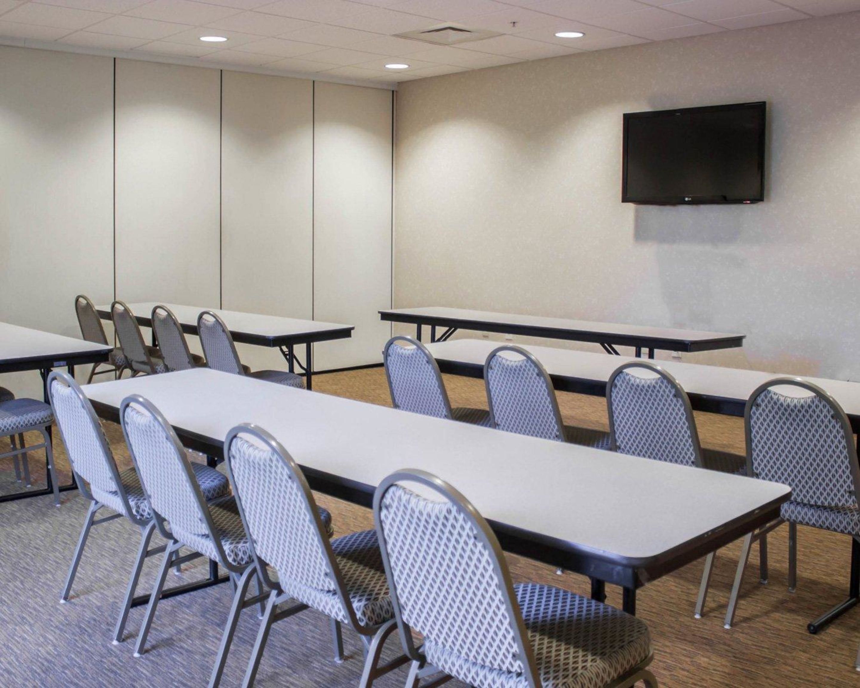 A conference room with long tables and chairs, a flat-screen TV on the wall, and a carpeted floor.