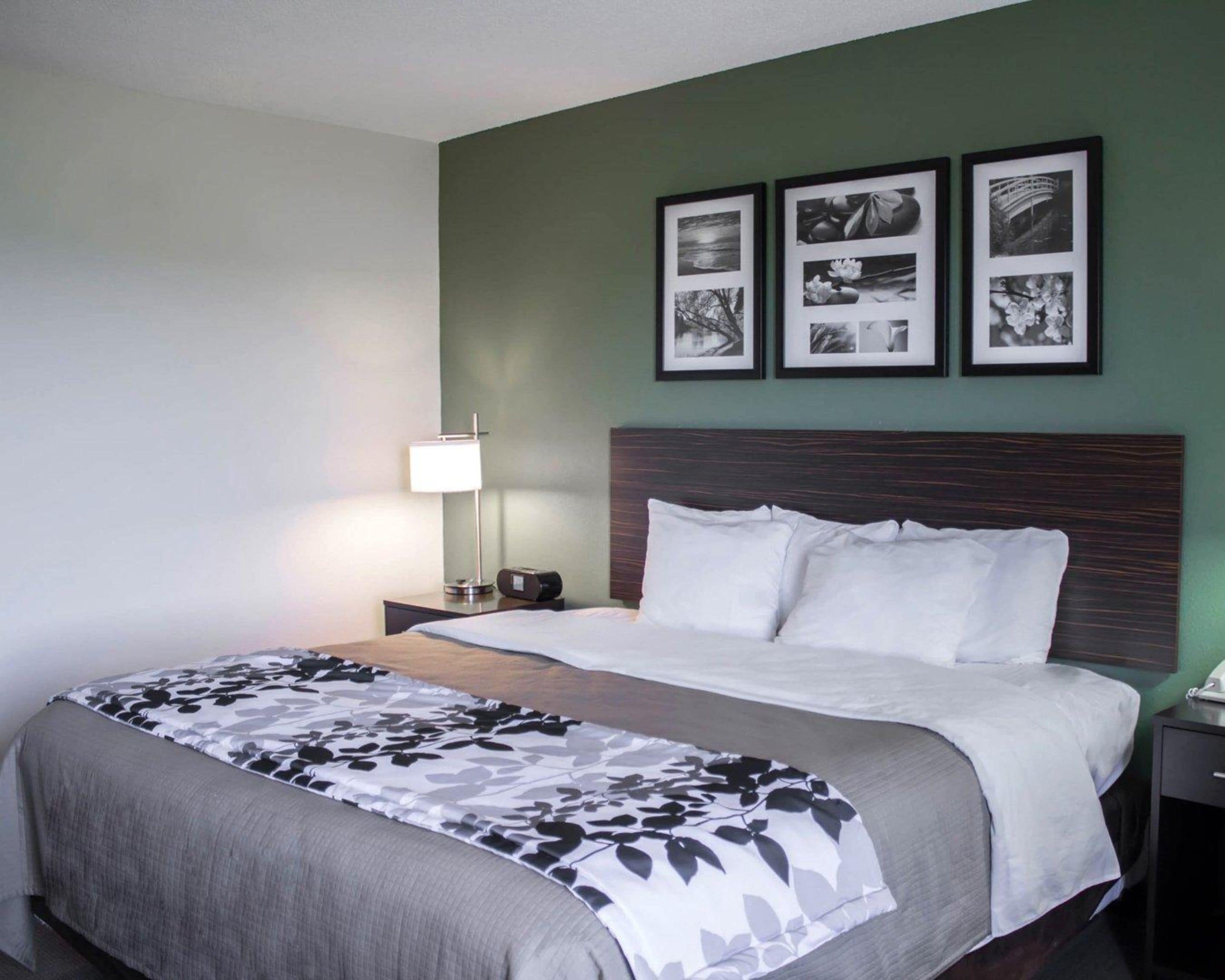A hotel room with a bed, a bedside table with a lamp, and three framed pictures on the wall.