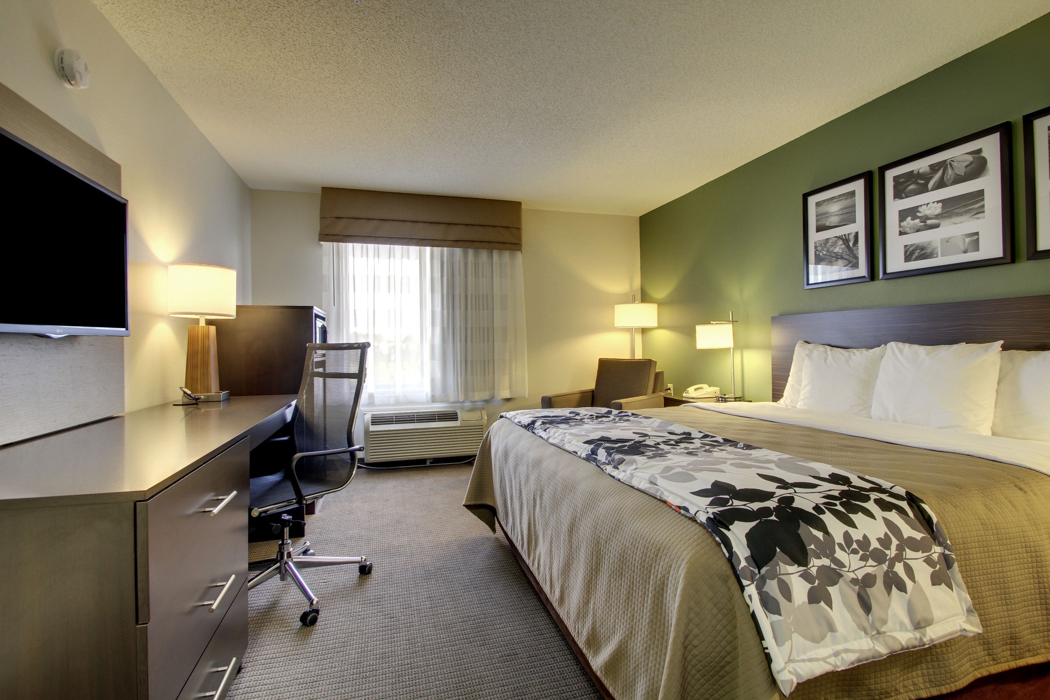 A hotel room with a bed, desk, chair, TV, and two lamps.