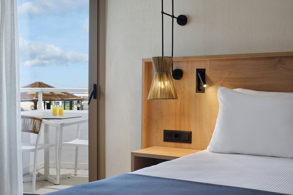 Une chambre d’hôtel moderne avec un grand lit, une tête de lit en bois, une table de chevet et une lampe suspendue.