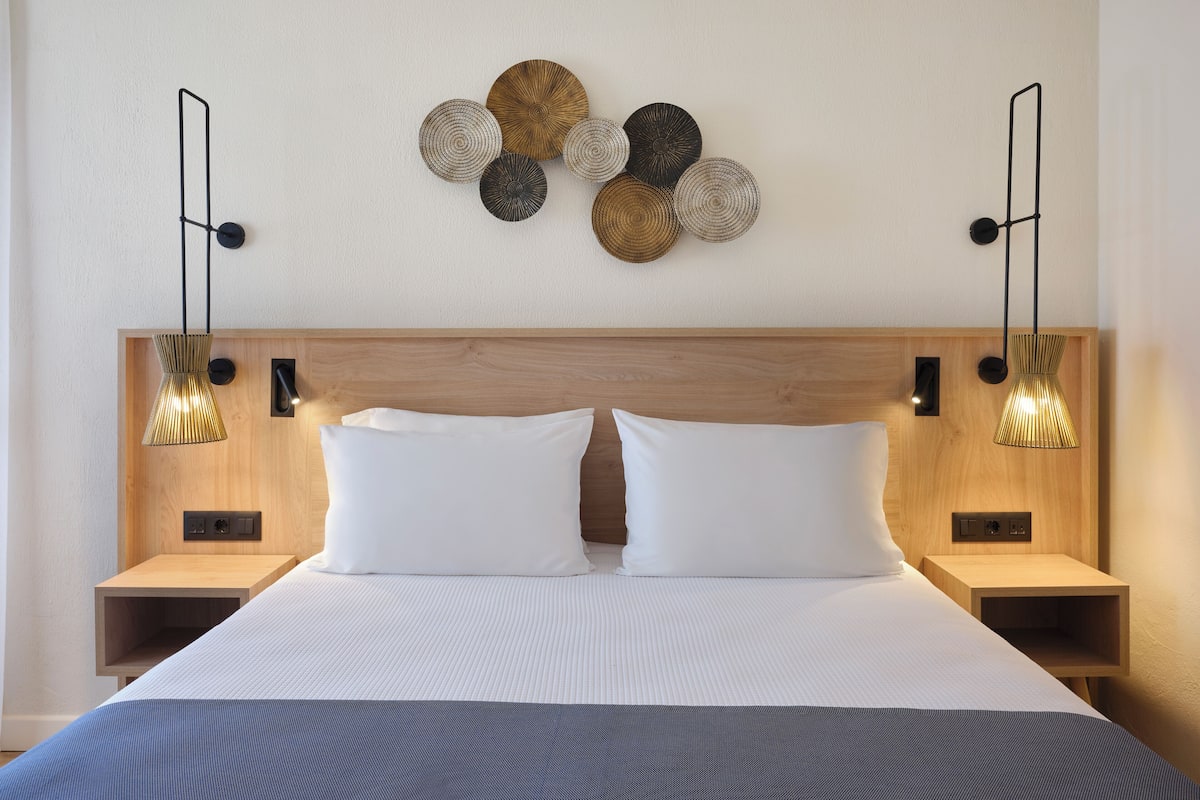 Un lit bien fait, avec du linge de lit blanc, deux tables de chevet avec des lampes et une tête de lit en bois.