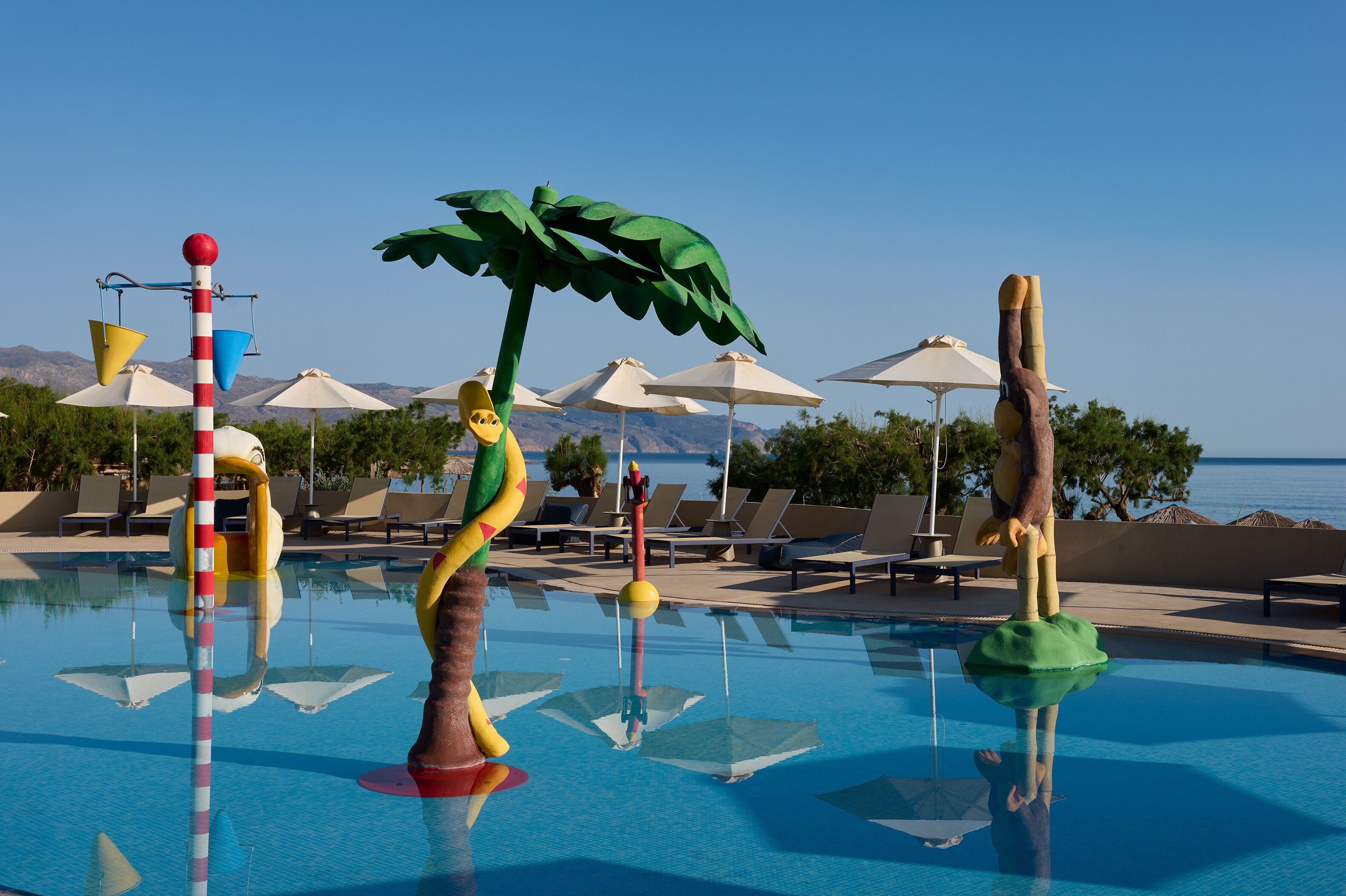 Un espace piscine avec des chaises longues et des parasols, un poteau décoratif et une vue sur la mer.