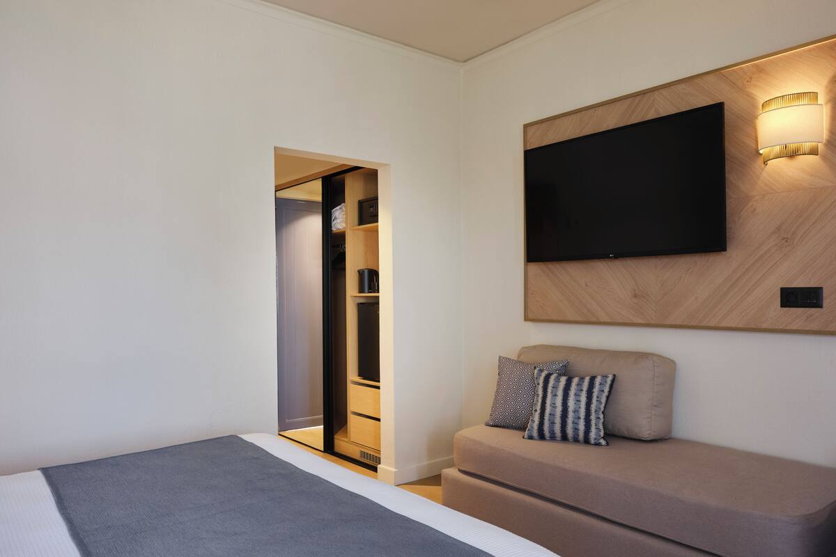 Une chambre d’hôtel moderne équipée d’un lit, d’un canapé, d’un téléviseur fixé au mur et d’un dressing.