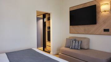 A modern hotel room with a bed, a sofa, a TV mounted on the wall, and a walk-in closet.