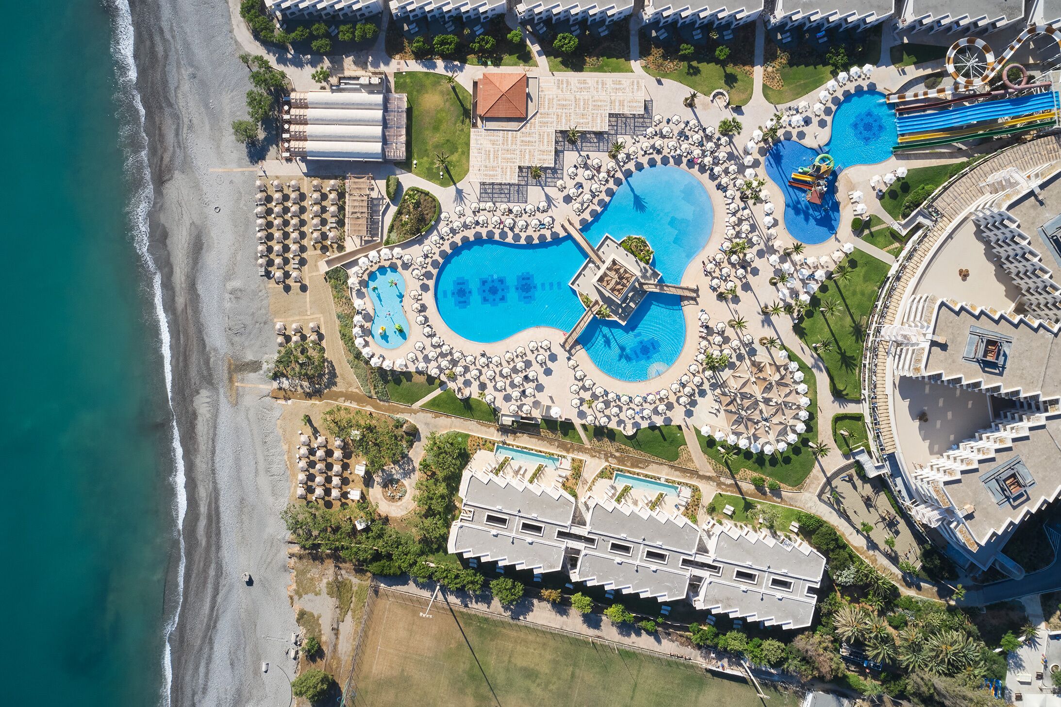 Eine Vogelperspektive zeigt einen luxuriösen Kurort mit mehreren Schwimmbecken, Zugang zum Strand und den dazugehörigen Gebäuden.