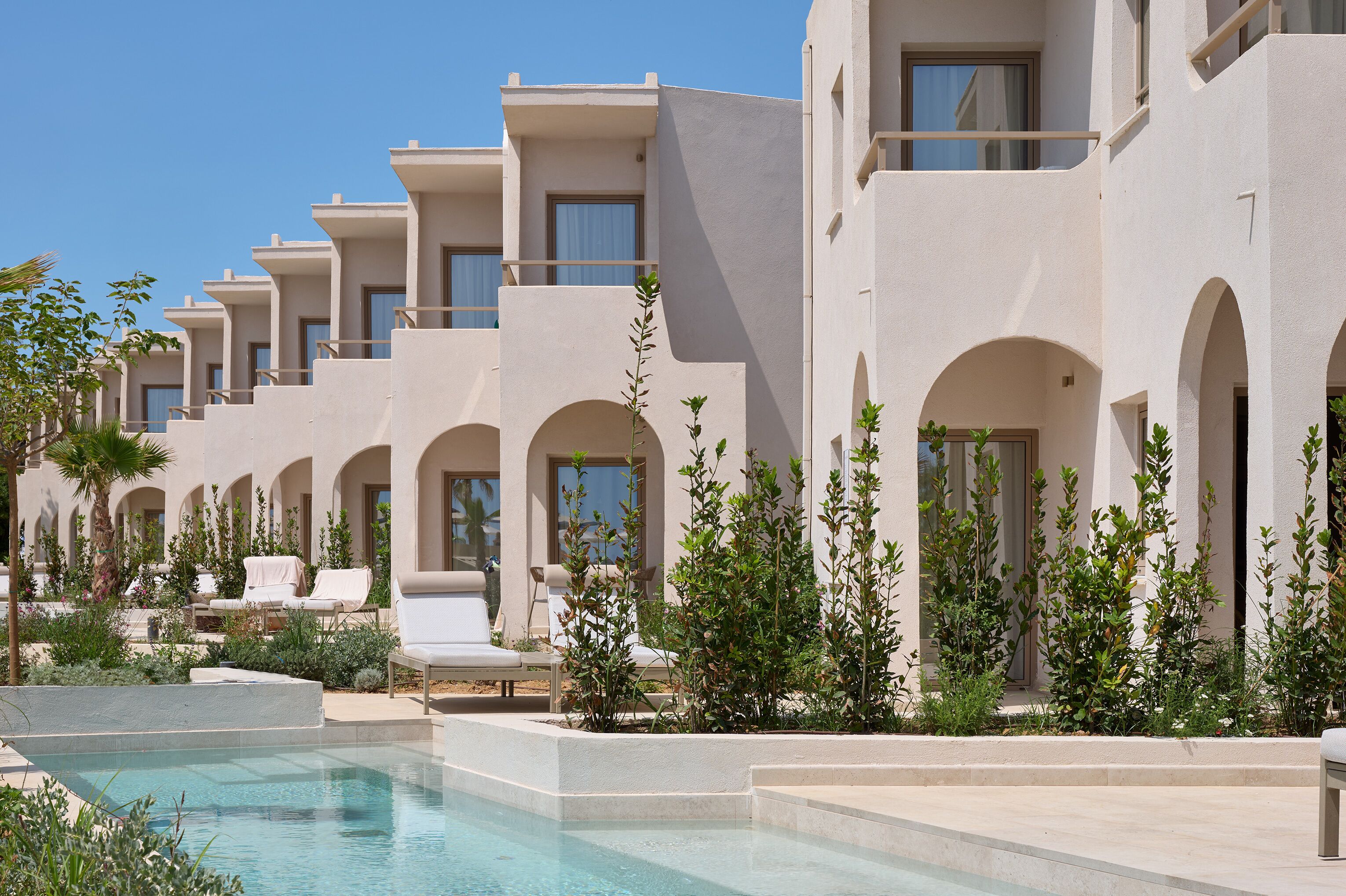 Un resort con varias edificaciones blancas, una piscina y sillones de descanso.