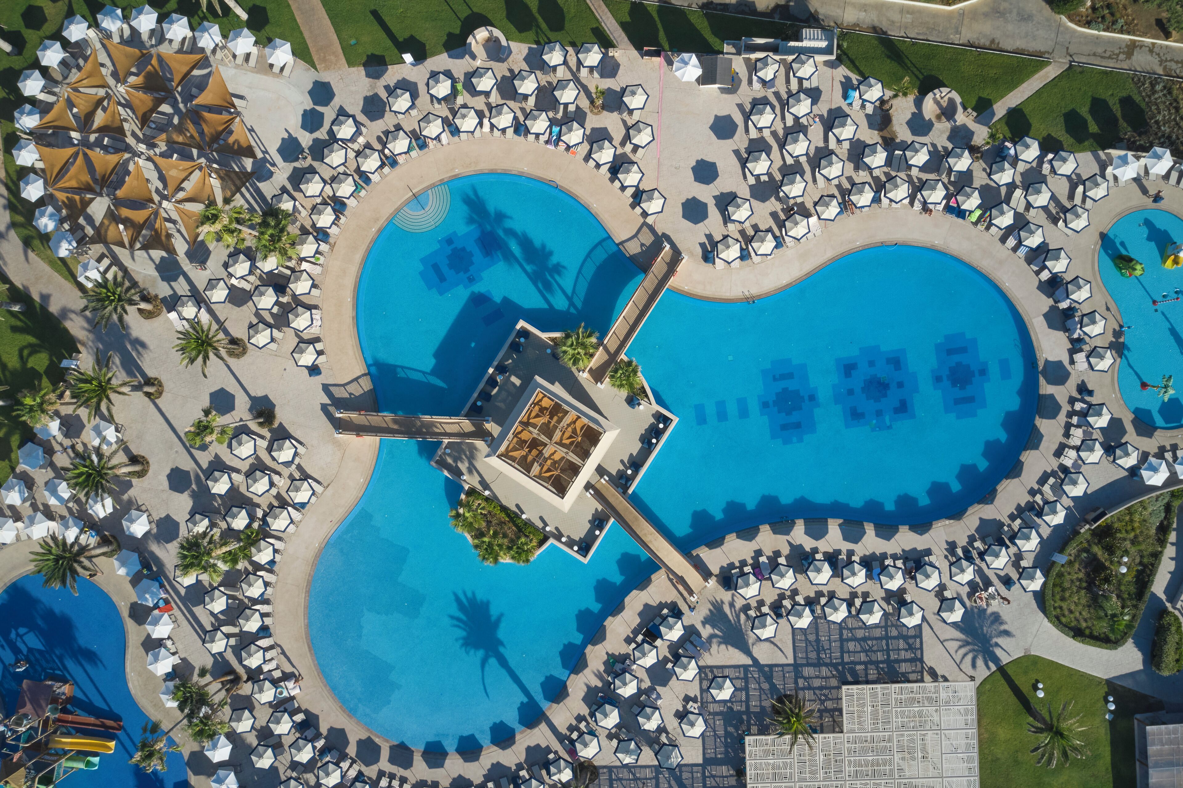 An aerial view of a resort with multiple swimming pools, sun loungers, and palm trees.