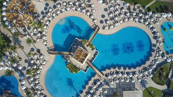 An aerial view of a resort with multiple swimming pools, sun loungers, and palm trees.