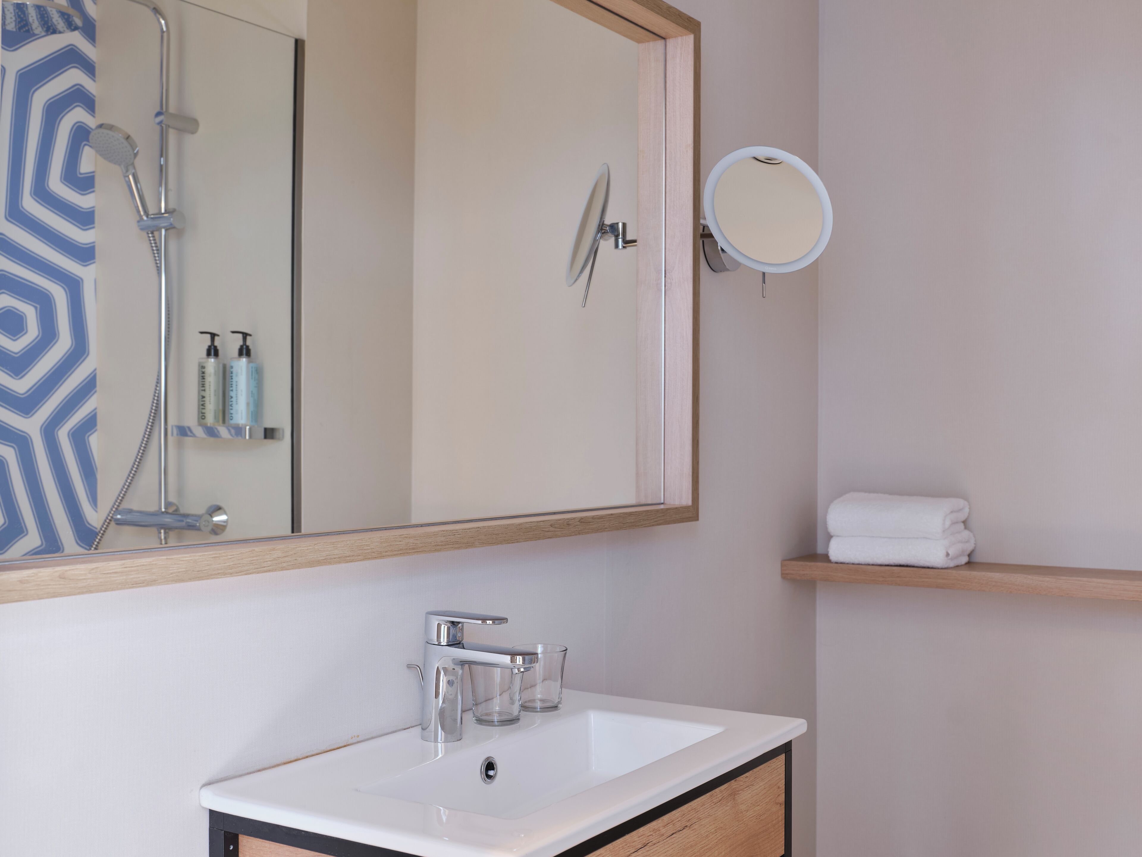 A bathroom with a white sink, a mirror, a shower, and a towel rack.
