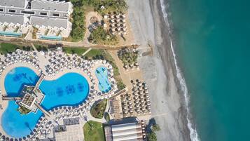 An aerial view of a resort with a large swimming pool, beach area, and multiple guest rooms.