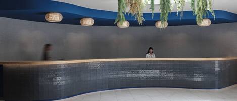 A modern reception desk with a curved design, a blue and grey color scheme, and hanging plants above.
