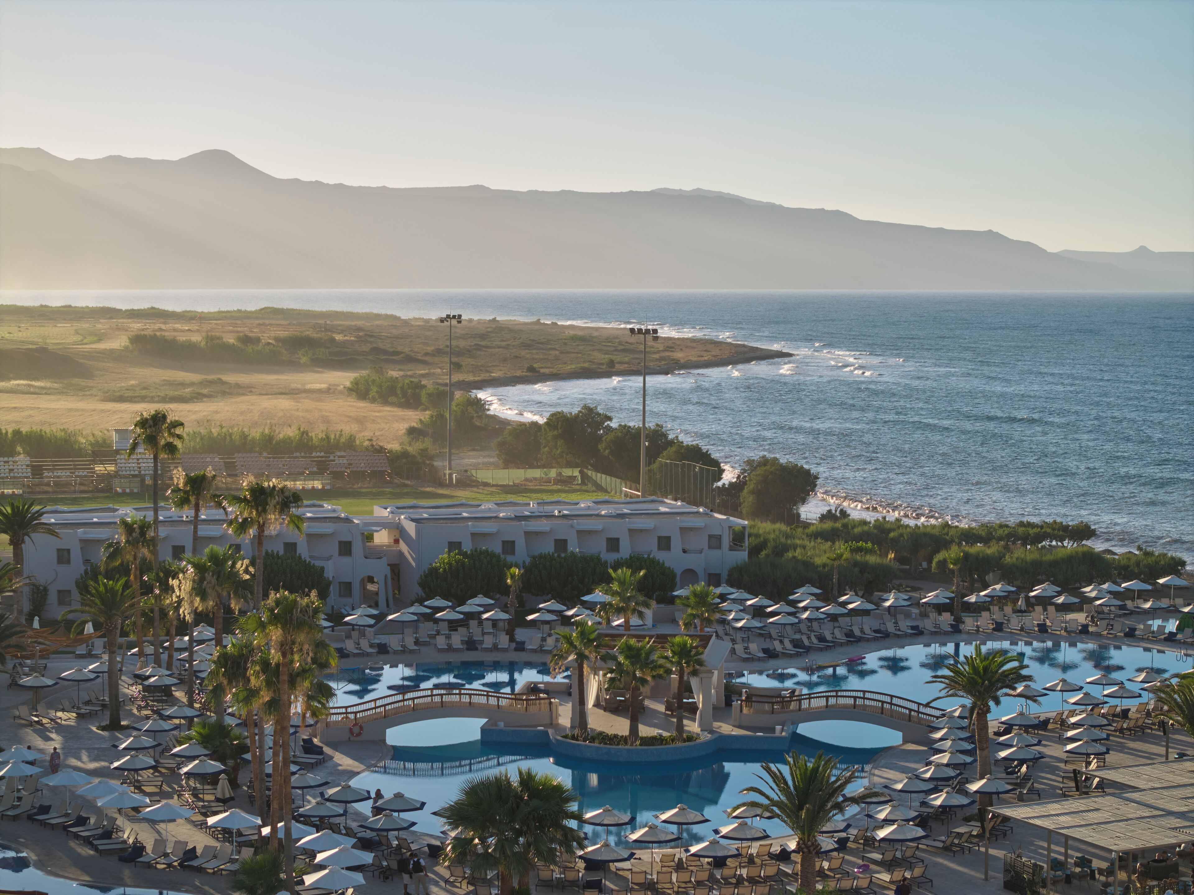 Un resort con varias piscinas, palmeras y vista al océano.