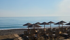 A beachside area with rows of lounge chairs and thatched umbrellas, overlooking the sea.
